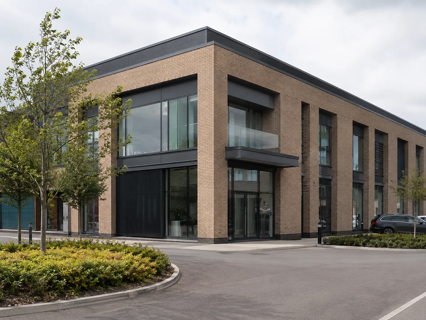 Two-storey commercial building in buff brick with dark grey window frames and a glazed corner entrance.