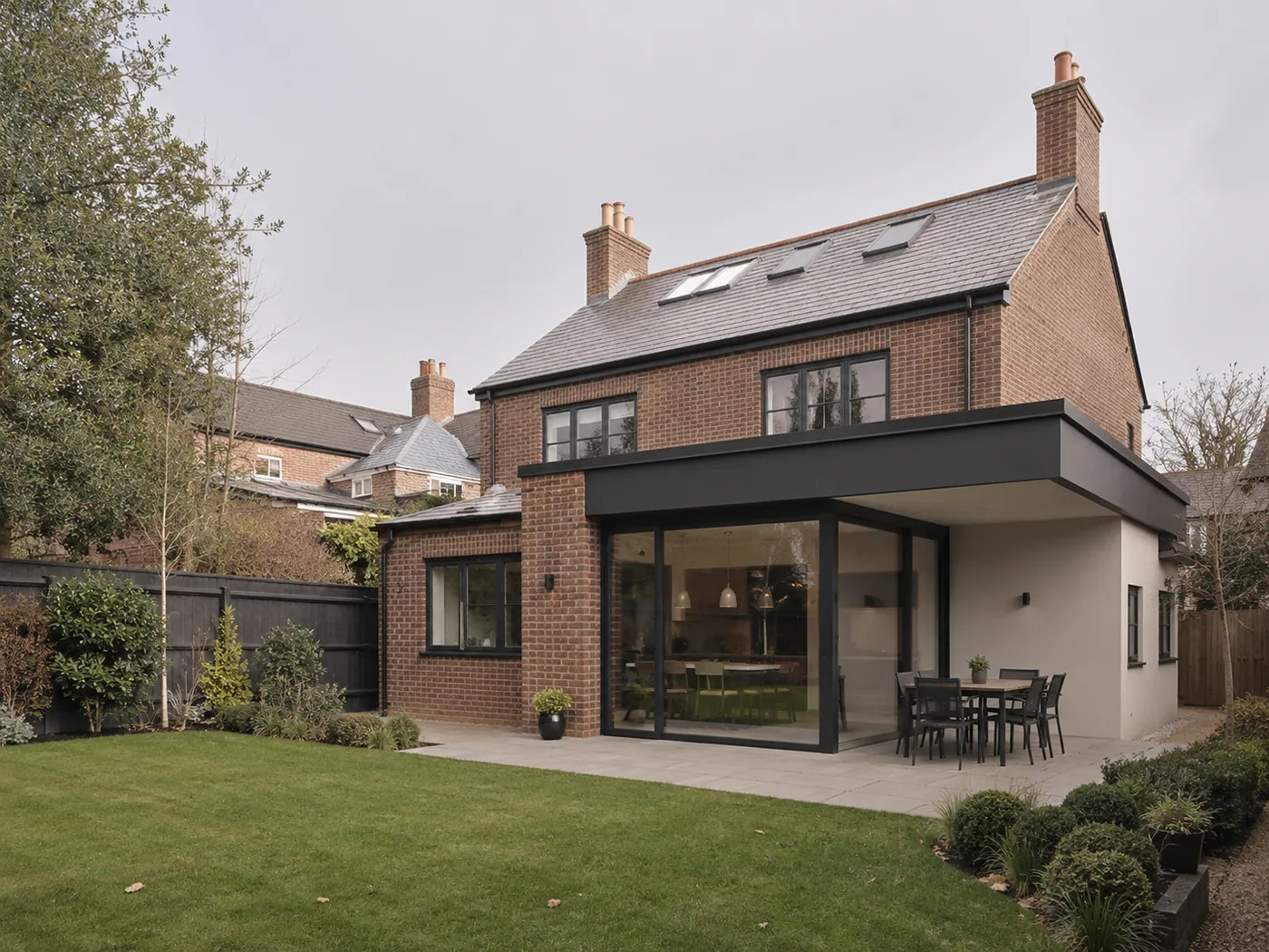 Detached brick house with a slate roof and a flat-roofed glazed rear extension onto a lawn.